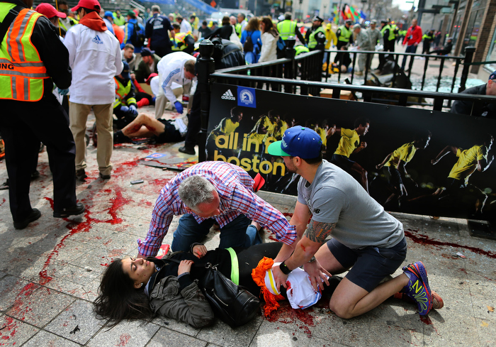 Boston-0415/13 Sydney Corcoran from Lowell is helped by Matt Smith (left) from Boston and Zack Mione from Portland Oregon on the sidewalk at the site of the first Boston Marathon bombing. They saved her life by using t-shirts around her legs and applied pressure to stop the bleeding. A piece of shrapnel from the pressure-cooker bomb the size of a cell phone severe her femoral artery. Her mother Celeste lost both legs.