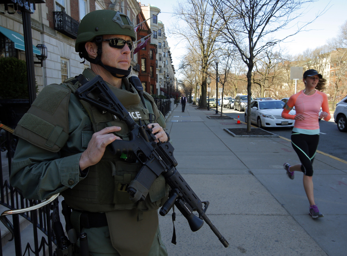A woman jogs past a police officer in tactical gear guarding the entrance to a hotel in Boston, Massachusetts April 17, 2013. Two explosions hit the Boston Marathon as runners crossed the finish line on Monday killing at least three people and injuring over 100 others.