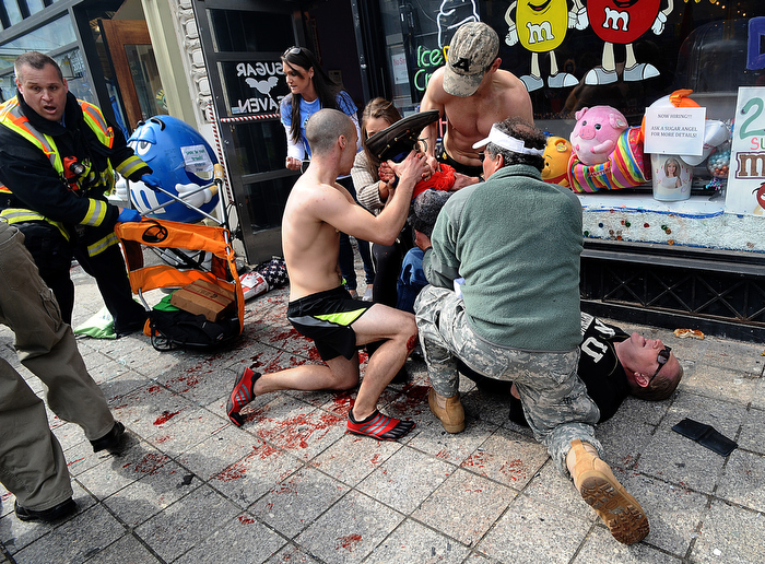 Boston marathon runner Robert Wheeler of Ashland, a student at Framingham State University, kneeling at left, helps a man injured after the bombings at the Boston Marathon finish line. Wheeler had just crossed the finished line and ran to the scene of the first bombing, taking off his shirt to apply it to the man's wound and elevating the leg in an attempt to slow the bleeding.