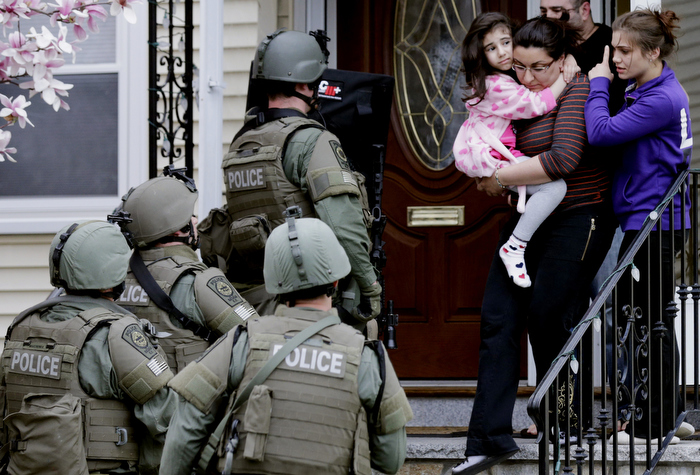 A woman carries a girl from their home as a SWAT team searching for a suspect in the Boston Marathon bombings enters the building in Watertown, Mass., Friday, April 19, 2013.