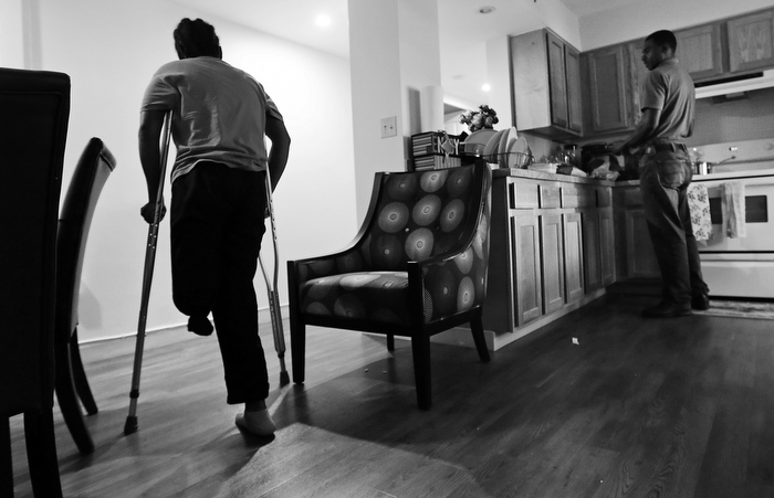 Mery Daniel, a Boston Marathon bombing survivor, uses crutches as she heads down a hallway in her home, while husband Richardson Daniel helps prepare dinner, Thursday June 20, 2013, in the South End neighborhood of Boston. Richardson Daniel, who had been a dermatologist in Haiti, works with a group helping Autistic children in Boston. With his wife coping with her physical changes, Richardson has had to increase his other responsibilities in their family.