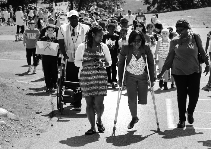 Mery Daniel, a Boston Marathon bombing survivor, uses borrowed crutches as she walks with students during a fundraising walkathon for her, at the William Seach Primary School in Weymouth, Wednesday, June 5, 2013. Students at the school raised over $8,000 for Daniel, whose father Hary Volmar, pushing wheelchair, is one of their bus drivers. Flanking Daniel is her mother, Marie Daniel, at right, and cousin Yvrantz Celestin, at left.