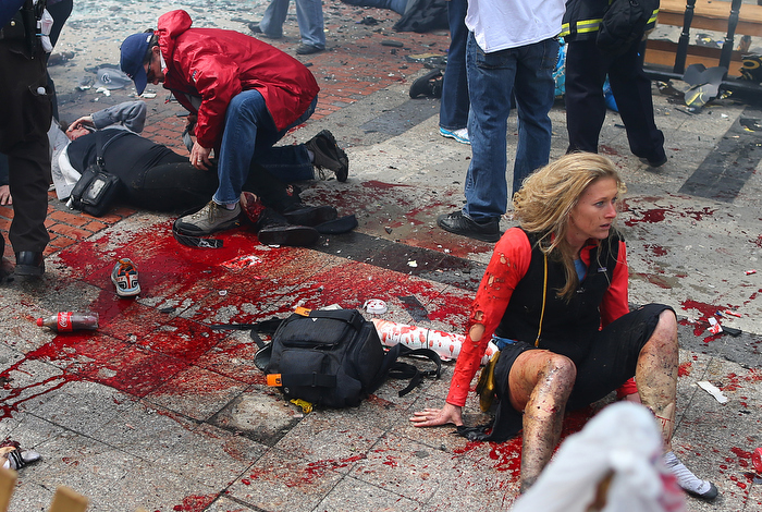 Boston-4/15/13- Kevin Corcoran (left) from Lowell puts his belt on the leg of his wife Celeste to stop the bleeding, as Nicole Gross (rt) from Charlotte, N.C. sits in shock on the sidewalk at the site of the first Boston Marathon bombing near the finish line on the Boylston Street.