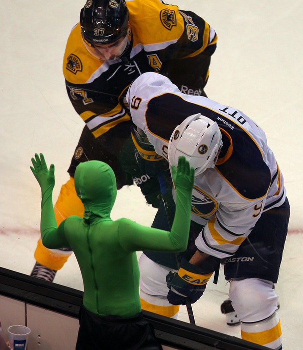 Boston-01/30/13- Bruins Patrice Bergeron fights for a loose puck against the board with Buffalo Steve Ott as a fan dressed in a green outfit bangs on the glass in the 1st period.