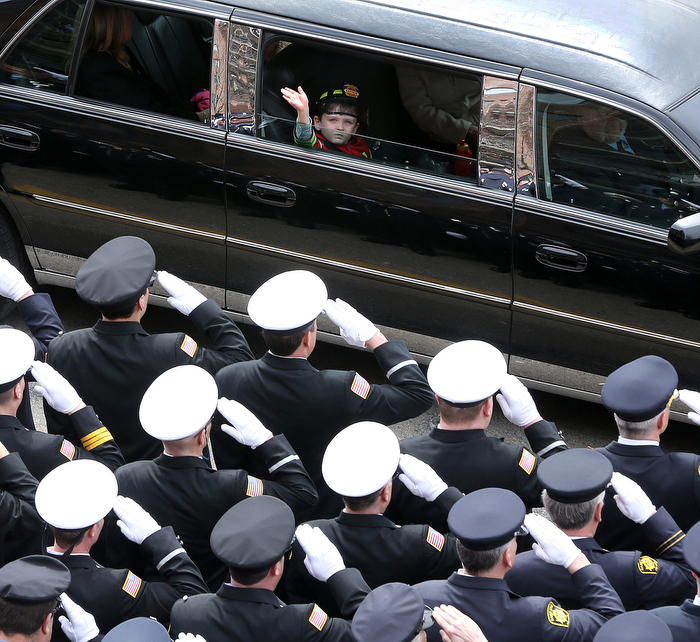 On the way to the cemetery, a young "captain" waves to the crowd. The funeral for Boston Fire Lt. Edward J. Walsh, Jr. is held in Watertown, on Wednesday, April 2, 2014.